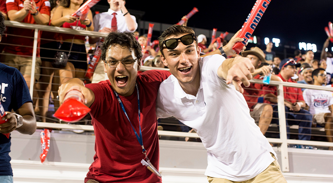 Two male ֱ during an FAU football game smiling and pointing at the camera
